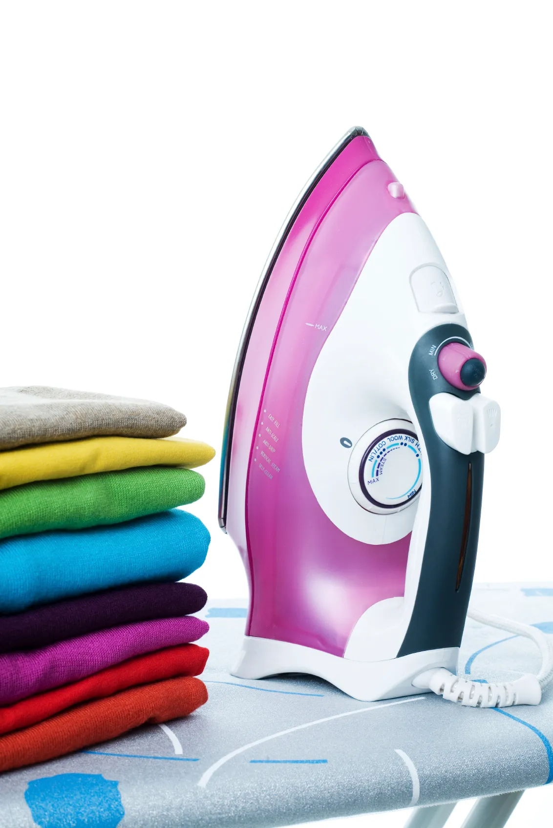 A steam iron standing on an ironing board next to a stack of folded, brightly coloured jumpers